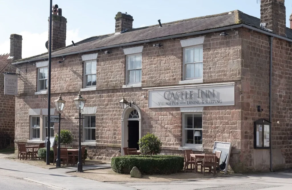 A shot of the Castle Inn's exterior. A smart looking brick building with some green shrubbery outside and a few tables and chairs.