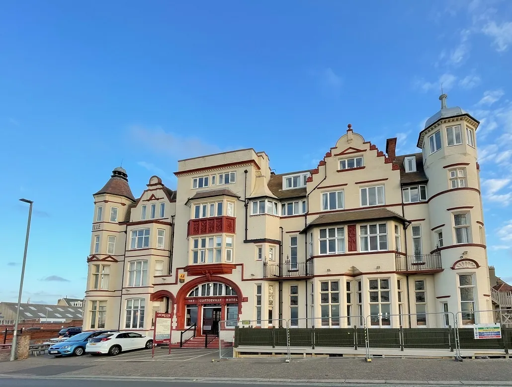 Exterior of The Cliftonville - a very large building with a couple of cars parked outside. Bright blue sky in the background. Best Pubs with Rooms in Norfolk.