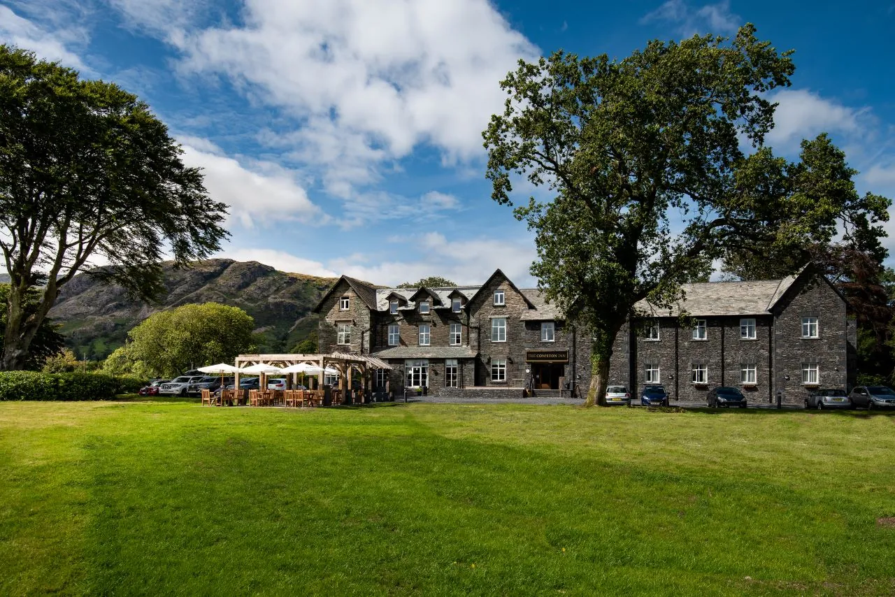 A huge garden with the Coniston Inn in the background. There are a few trees surrounding the Inn and a lovely nearby fell.