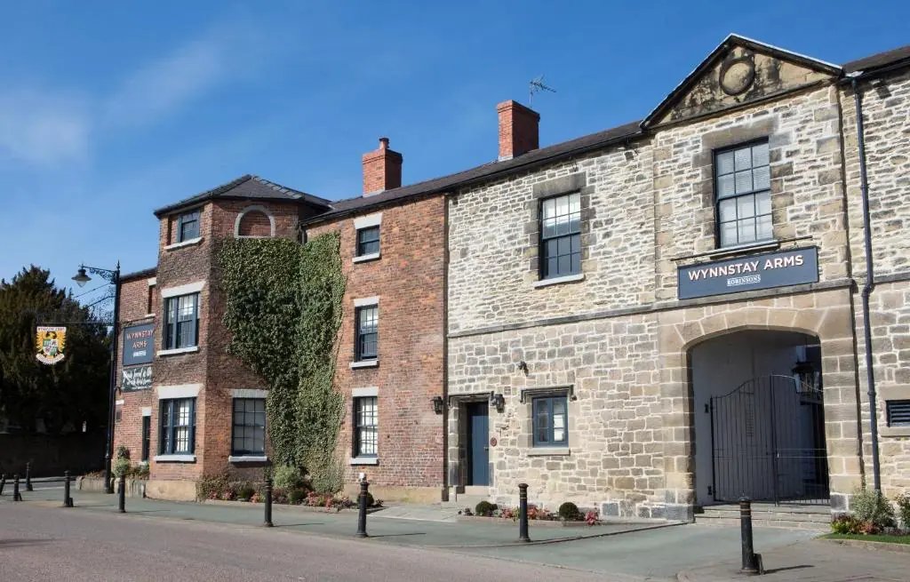 A large building with 2 signs which both say "Wynnstay Arms". There are multiple entrances, and green shrubbery along the side of the building