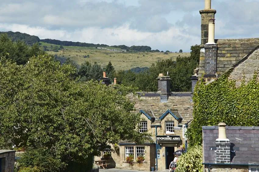 The front of the Devonshire Arms - beautiful landscape background. Building is somewhat hidden by trees, with the sign and front of building visible