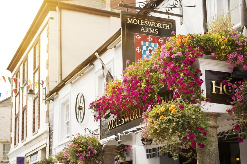 A white building with lots of pretty pink flowers and a sign stating 'Molesworth Arms'